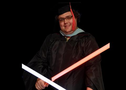 Photograph of Trevor Herald at his graduation, with light sabers