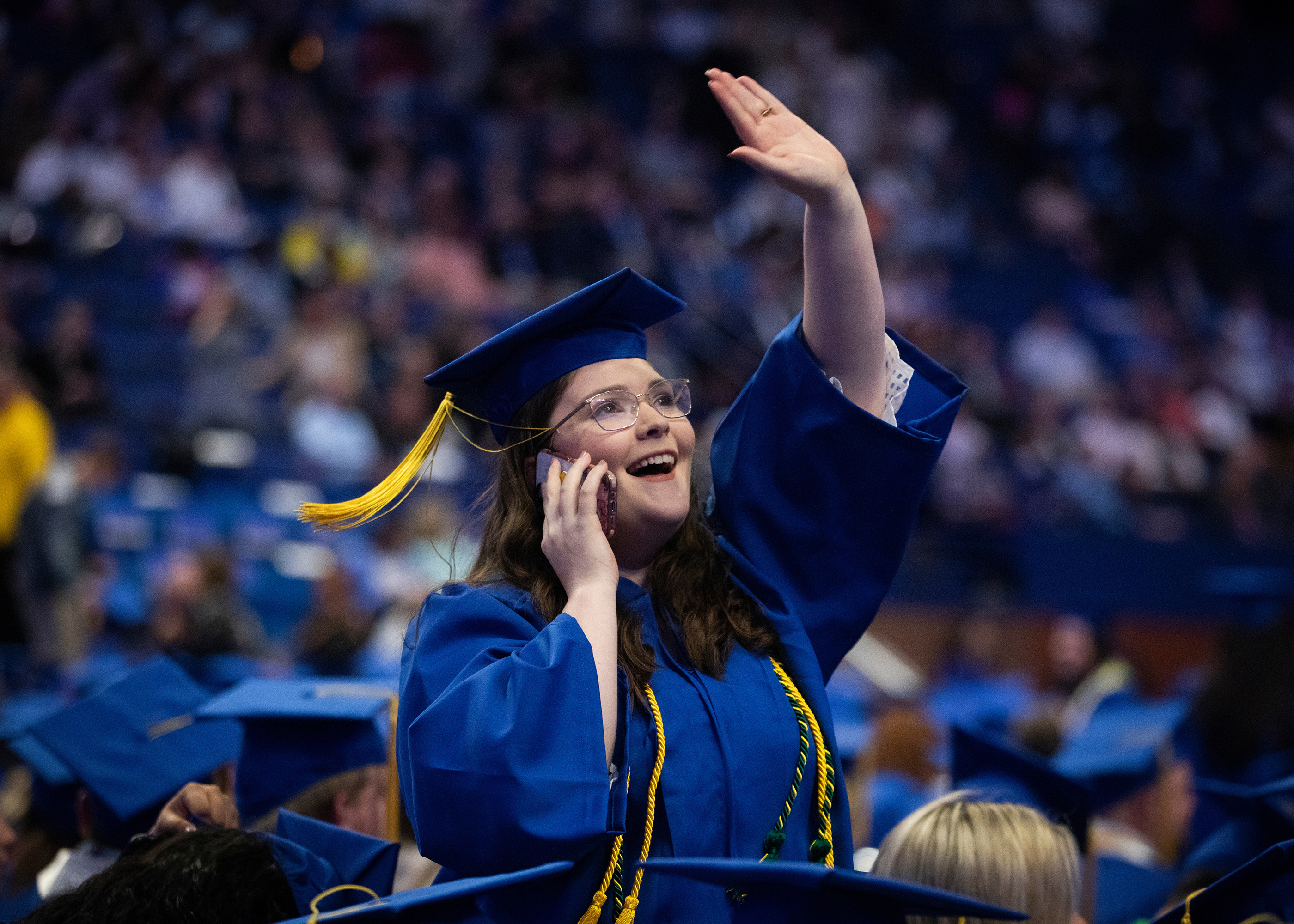 Student at graduation waving to family.