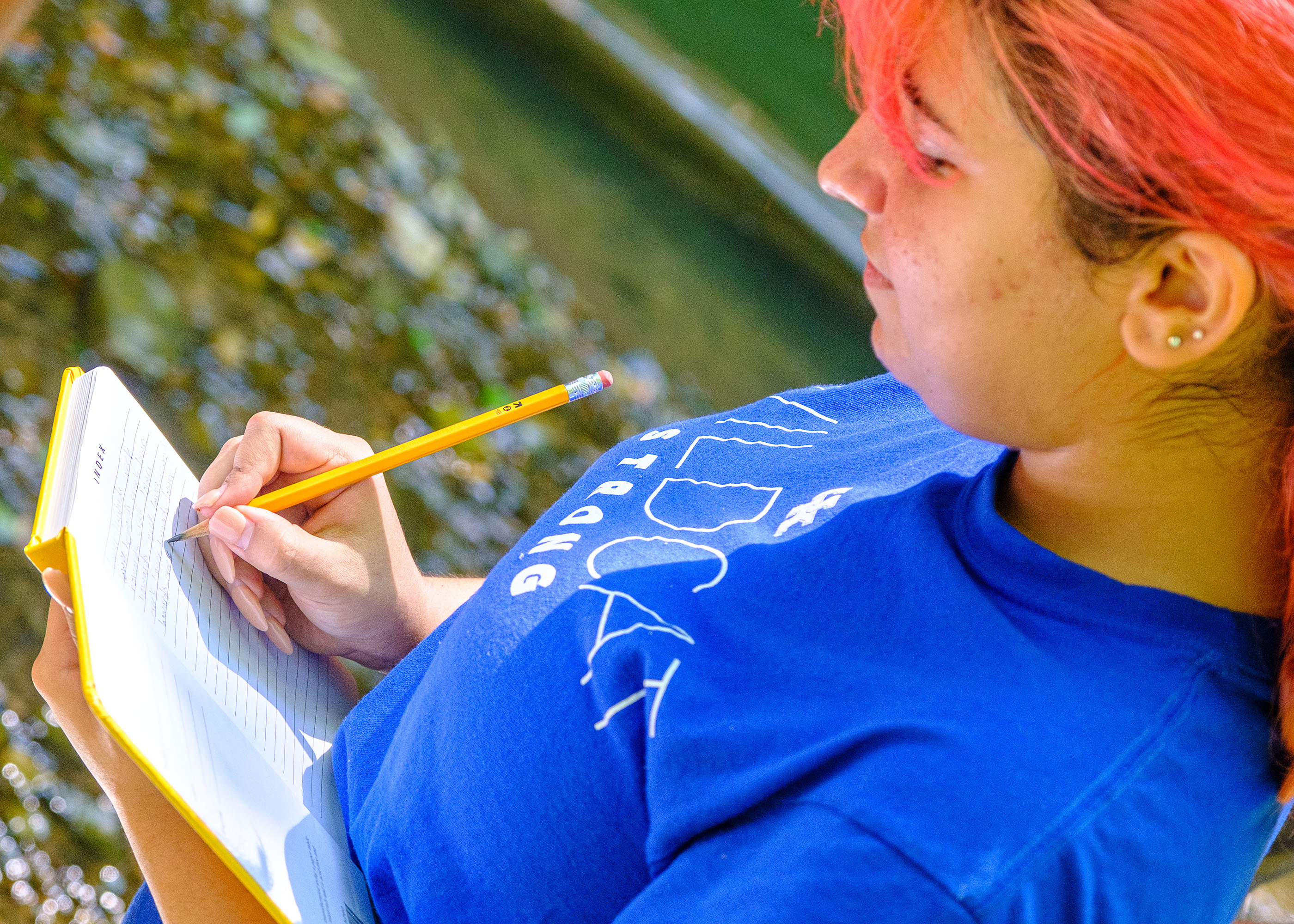 Student taking notes by a creek.