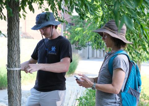 Photograph of student and faculty member taking tree measurements.